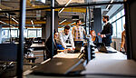 A group of young professionals collaborate in a modern office, with some using laptops and others discussing.