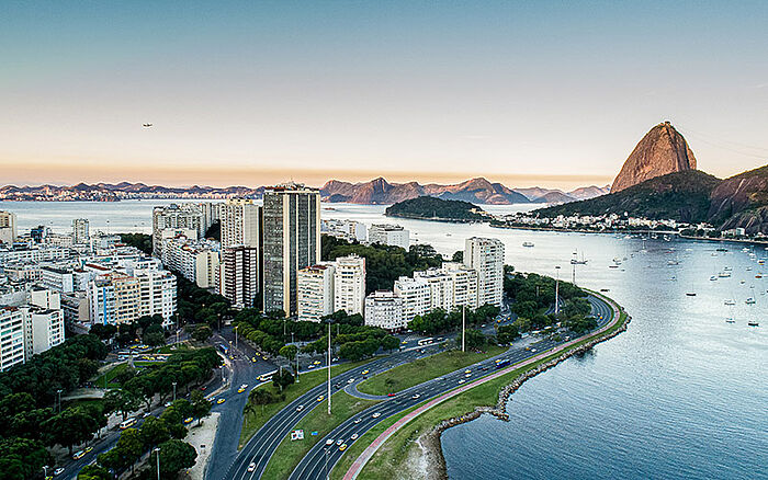 Aerial view of Flamengo Park at sunset, showing city buildings, roads, Guanabara Bay waters and Sugarloaf Mountain in the background, Rio de Janeiro, Brazil.
