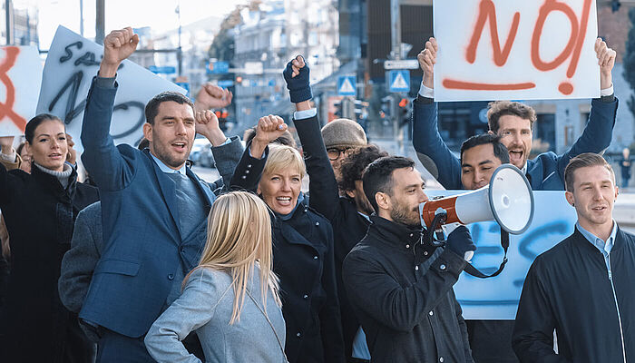 Multicultural group of office workers picketing on the street, holding signs and a megaphone in protest.