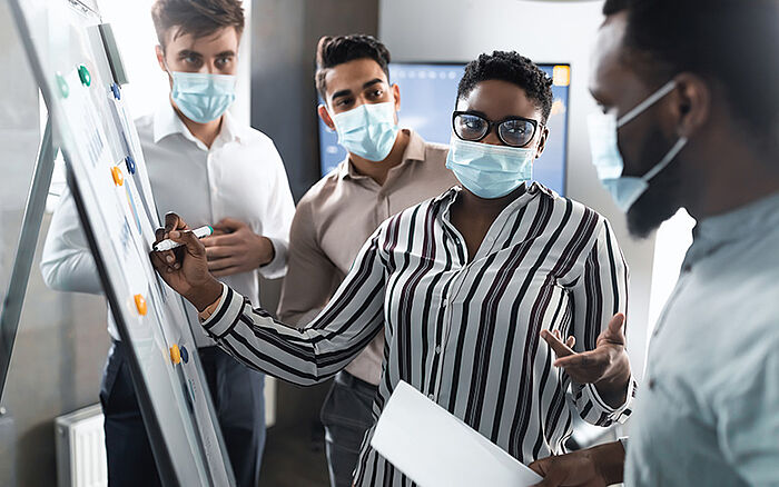 Employee wearing a medical mask presenting a business strategy on a whiteboard in an office setting.